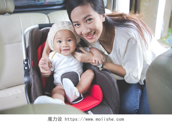 母亲在他的车上用汽车座椅保护婴儿微笑的小孩婴儿微笑